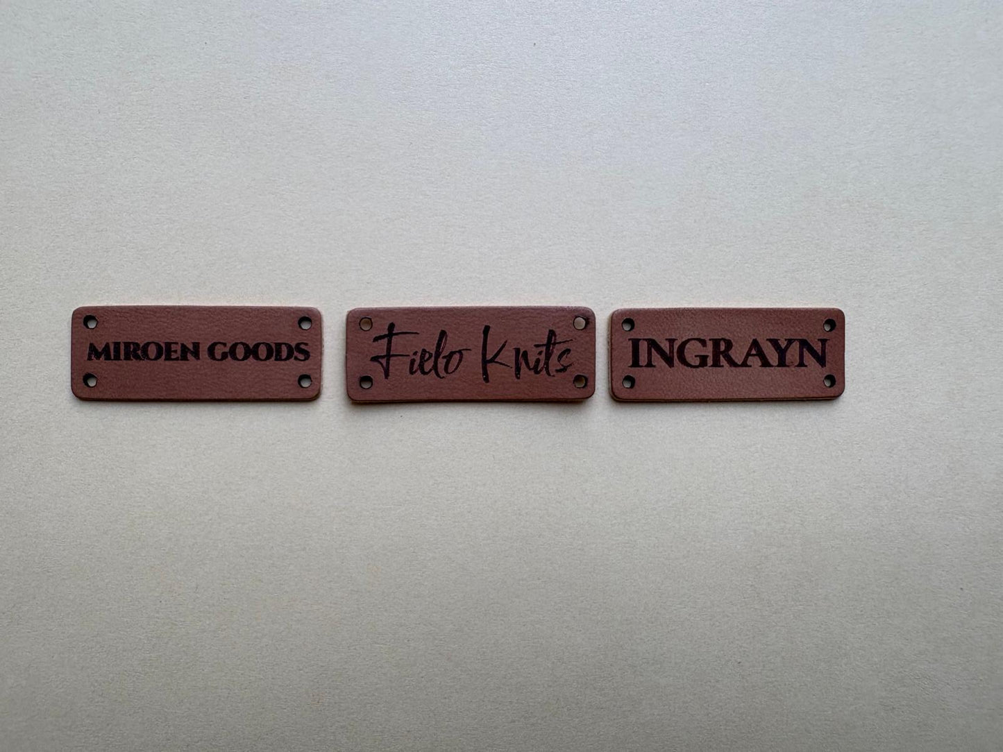 Drie kleine rechthoekige leren labels met verschillende designs
